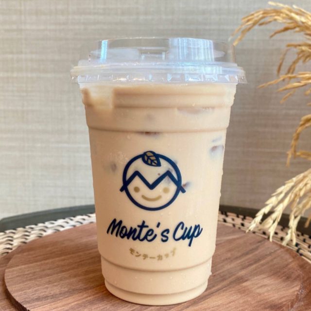 ชานมมอนเต้เย็นในแก้วใส มีโลโก้ Monte’s Cup พิมพ์บนแก้ว วางบนเขียงไม้