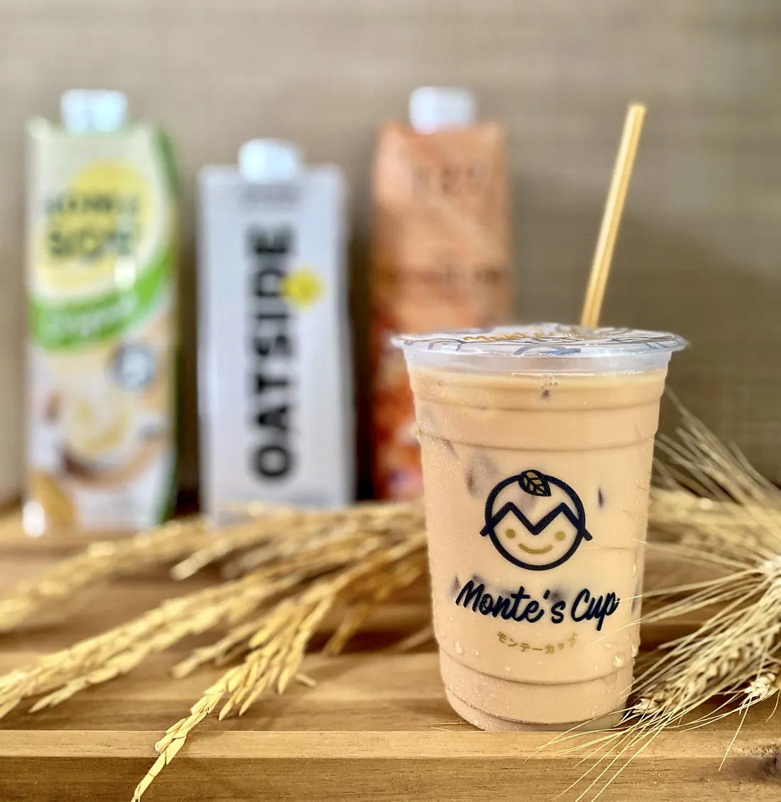 แก้วชานมมอนเต้เย็น มีโลโก้ Monte’s Cup พิมพ์บนแก้ว วางบนเขียงไม้กับรวงข้าว